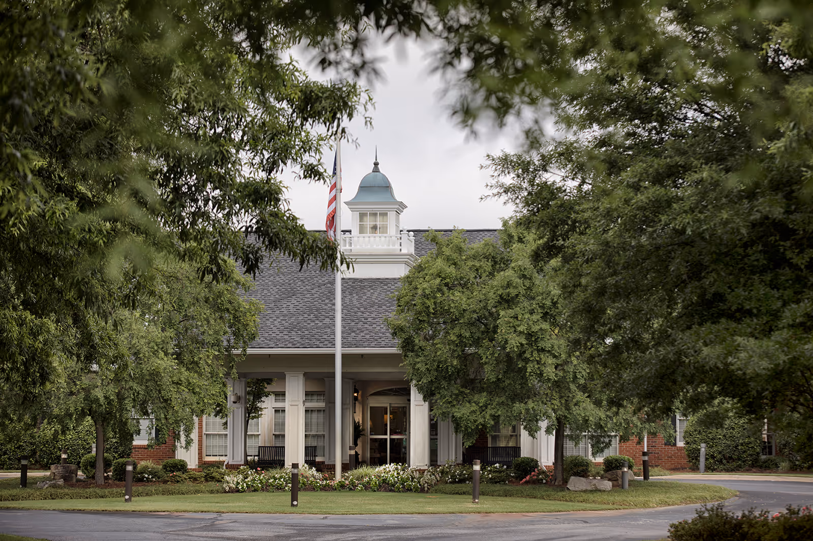 Exterior view of Wesley Woods of Newnan Peachtree City with entrance, flag, and trees.