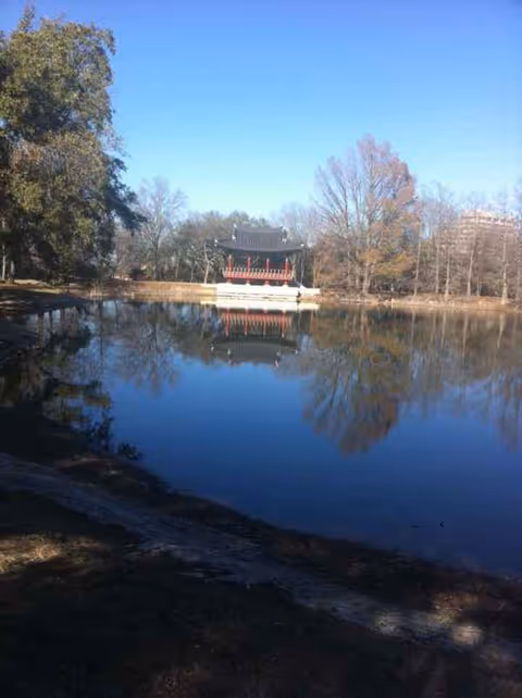 Serene lakeside scene with a pavilion on the water and surrounding trees.