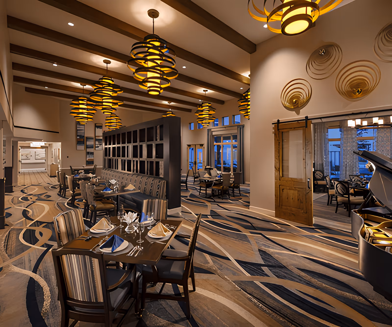 Large, elegant dining room with set tables and chairs, distinctive spiral pendant lights, patterned carpet, and a piano.