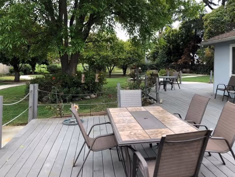 Outdoor wooden deck with a table and several chairs overlooking a grassy yard and trees.