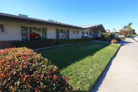 Single-story senior living facility exterior with manicured lawn and front sidewalk.
