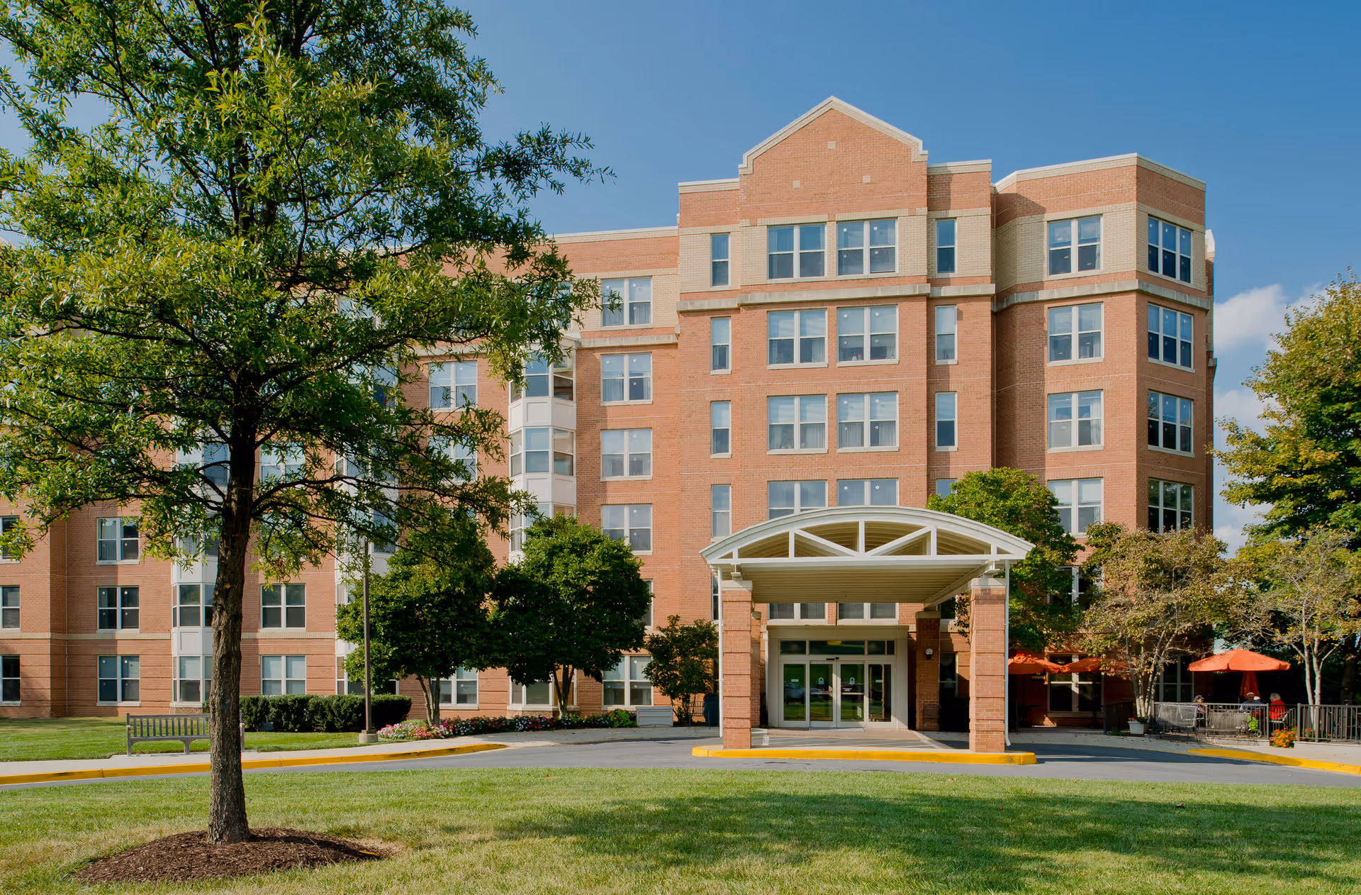 Exterior view of a brick senior living facility with a covered entrance and landscaping.