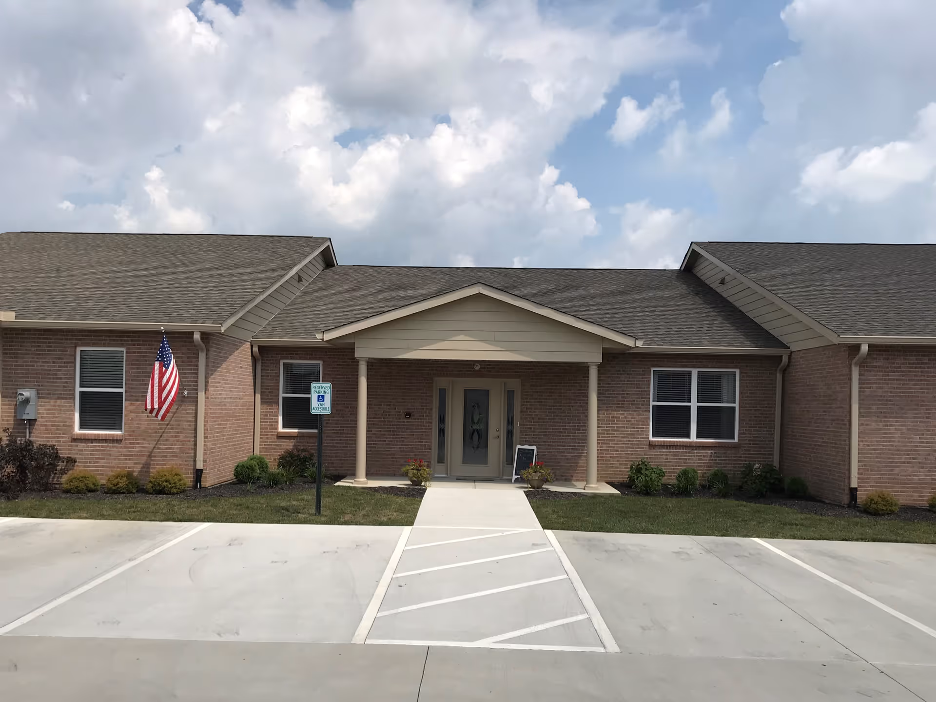 Single-story brick senior living building with a covered entrance and parking in front.