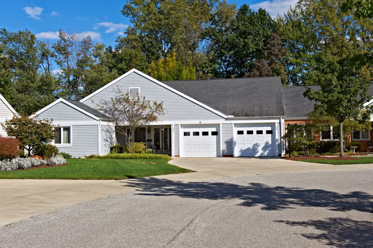 Single-story white siding residence with two garage doors, driveway, lawn and trees in front.