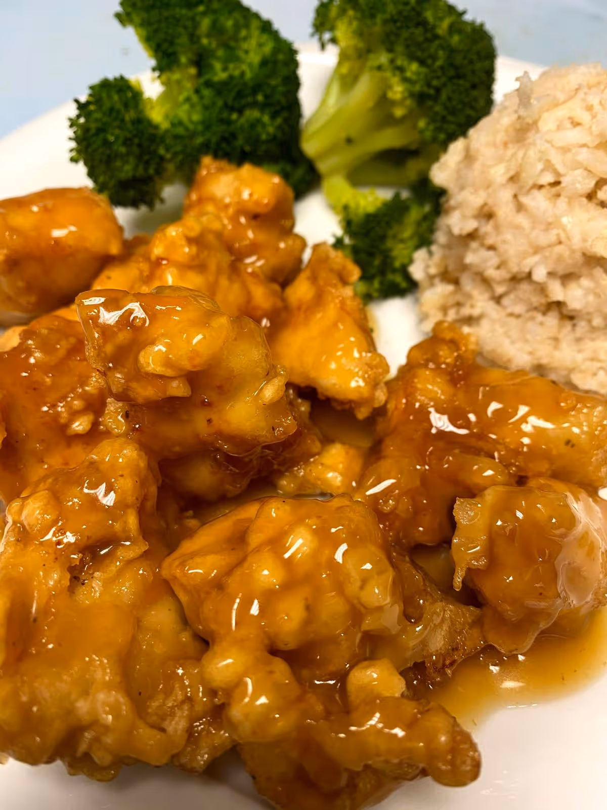 A close-up view of a plate with glazed fried chicken pieces, steamed broccoli florets, and a serving of brown rice.