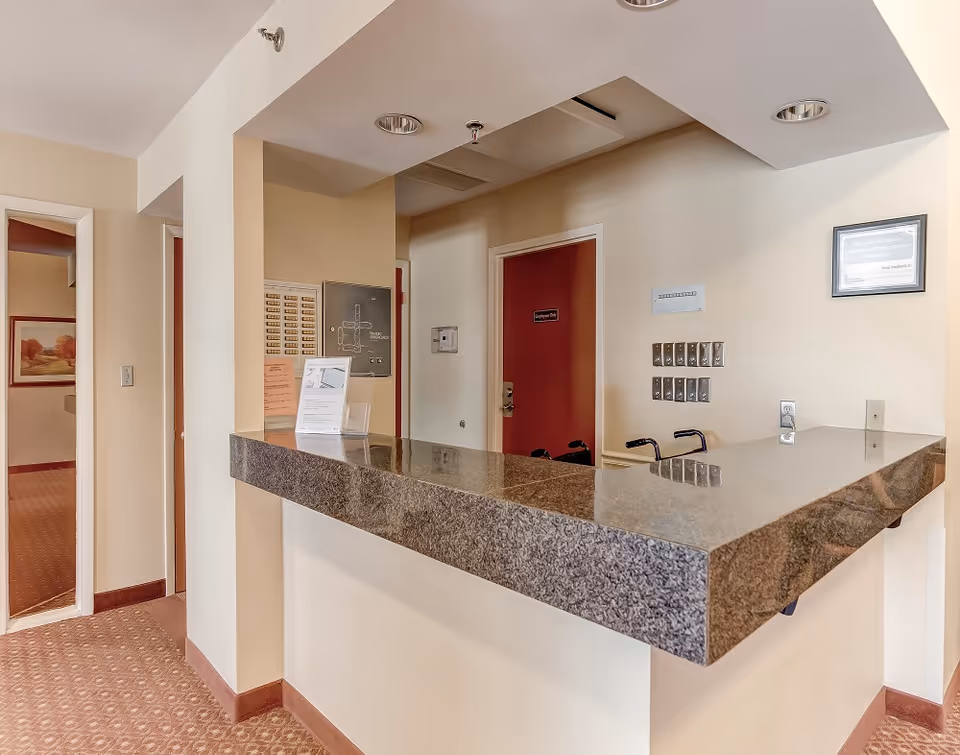 Reception counter with a dark granite top in an interior lobby area showing doors, key boxes, and informational signs.