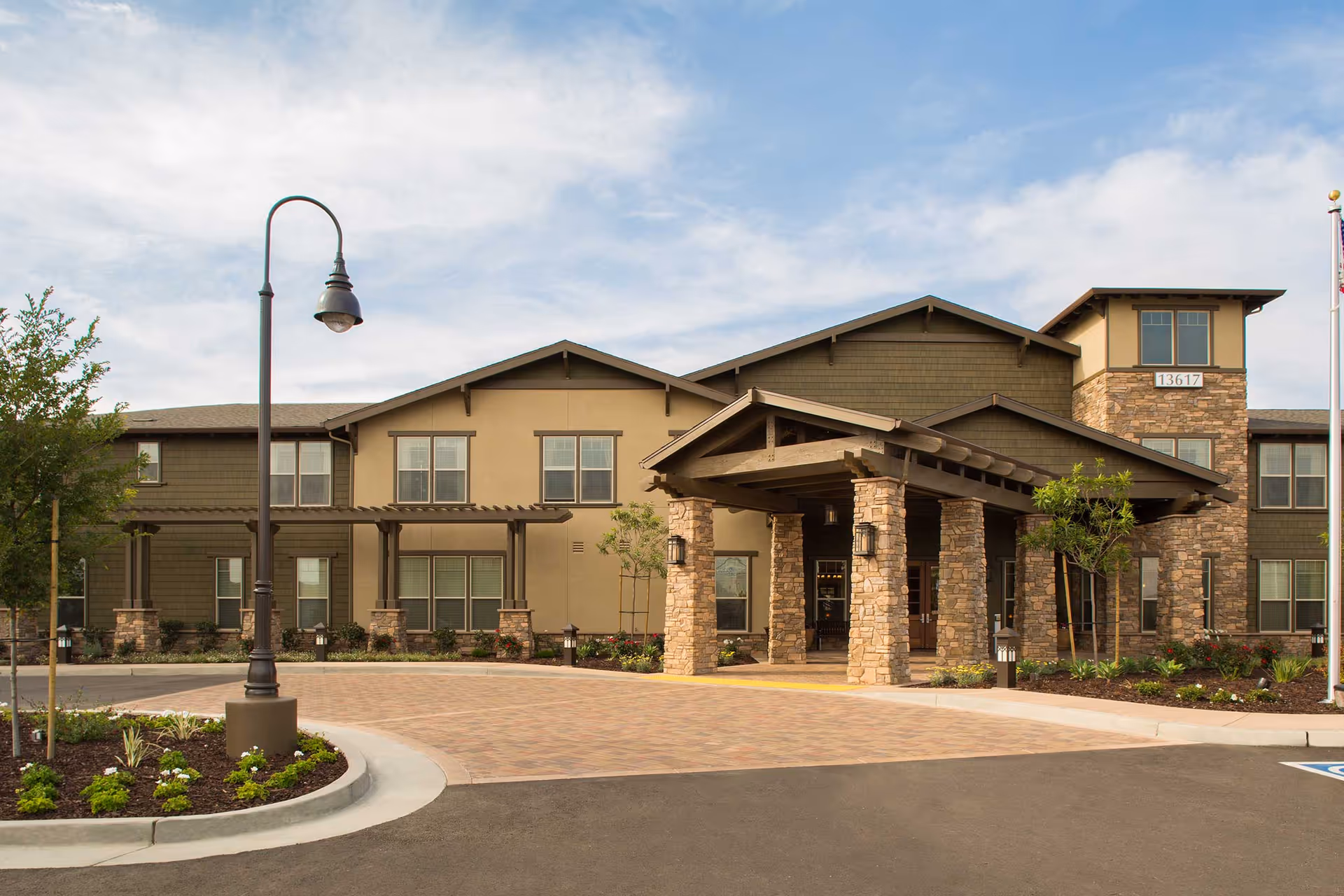 Front entrance of a two-story senior living building with a covered stone porte-cochère, landscaped driveway, and multiple windows.
