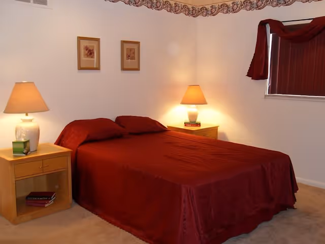 Bedroom in Sugarbush Living Woodkrest House with red bedding and lamps.