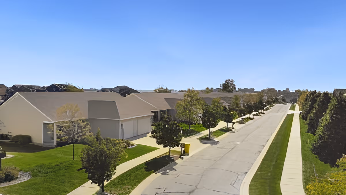 View down a tree-lined street with single-story residential buildings, sidewalks, and manicured lawns at a senior living community.