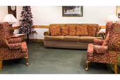 Lounge area with a sofa and two patterned armchairs, side tables with lamps, a small decorated Christmas tree, and framed art on the wall.