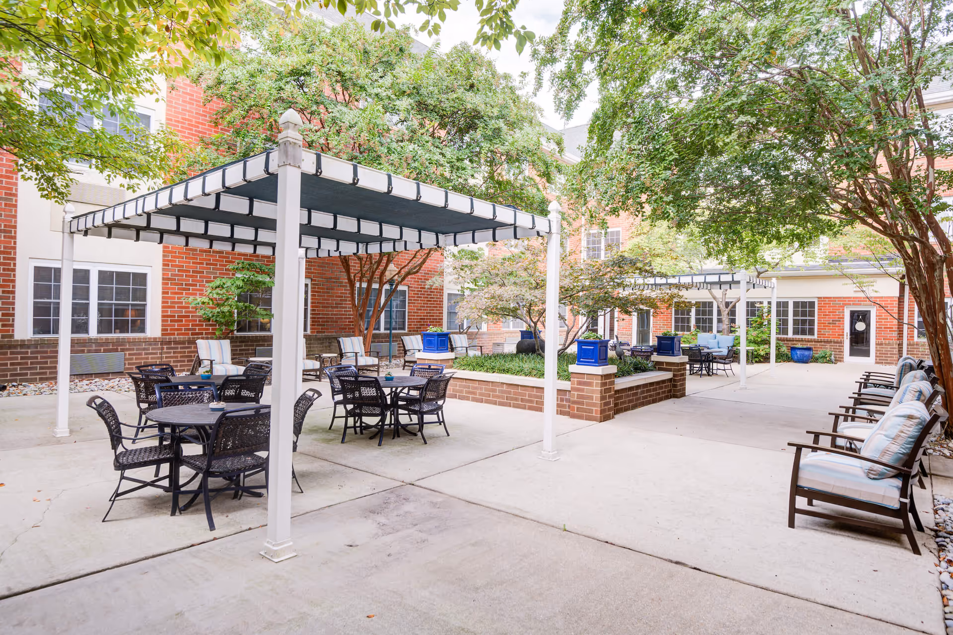 Outdoor courtyard with shaded seating areas, tables, brick planters and trees next to the building.
