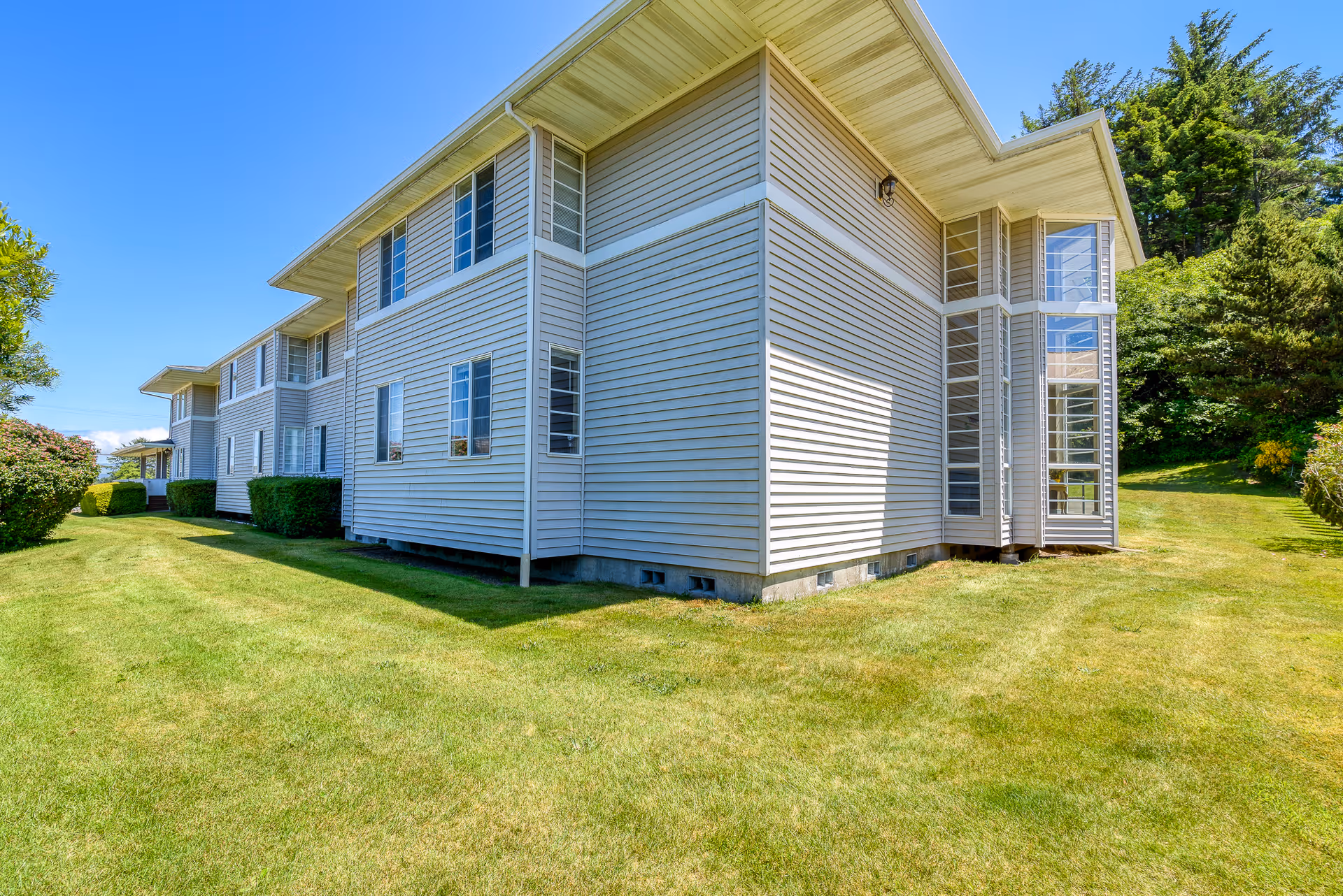 Exterior view of a two-story building with light-colored siding, multiple windows, and a well-maintained grassy lawn surrounding it under a clear blue sky.