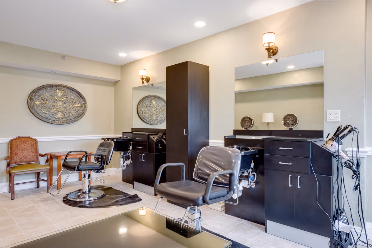 Interior salon area with two styling chairs, mirrors, black cabinetry, and decorative wall medallions.