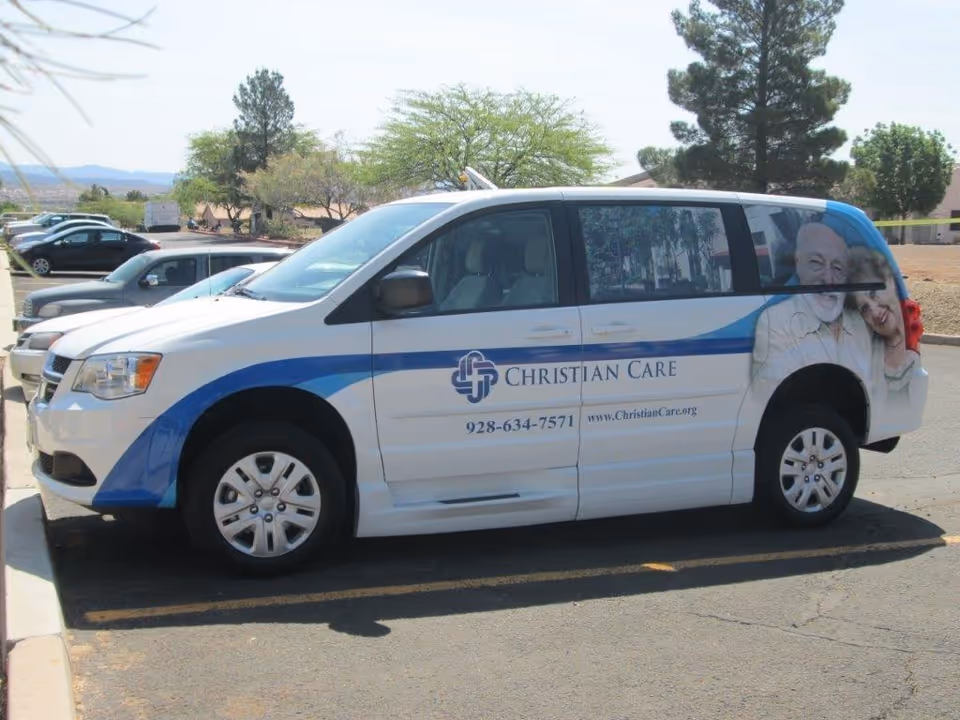 A white Christian Care branded van parked in a lot with the logo, phone number and a photo of an elderly couple on its side.