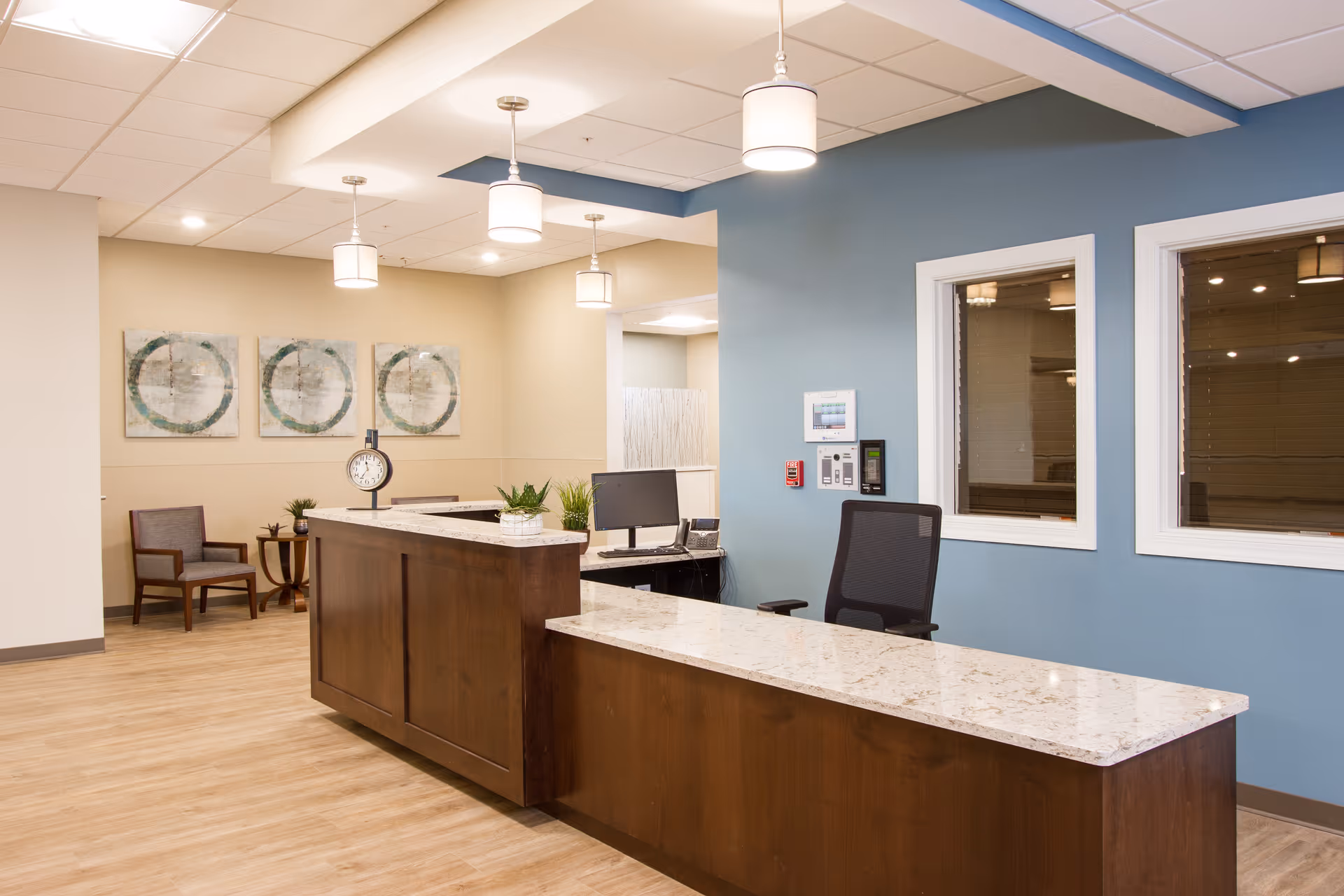 A reception desk with a marble countertop, office chair, pendant lights, and seating in a bright lobby.