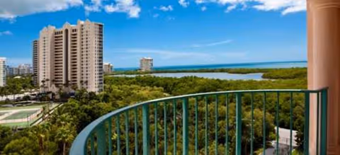 Balcony view from Premier Place overlooking ocean, trees, and nearby buildings.