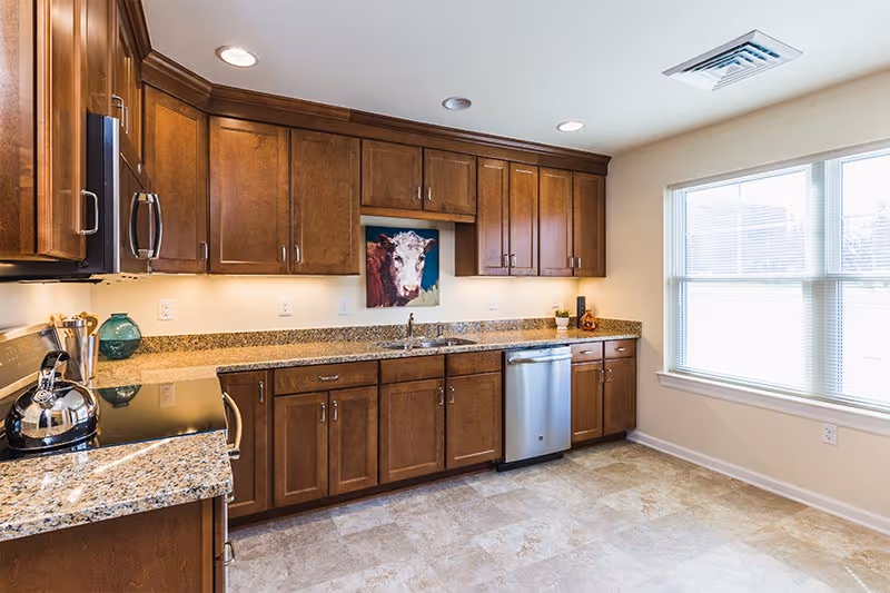 Bright kitchen with wooden cabinets, granite countertops, stainless steel appliances, and a large window.