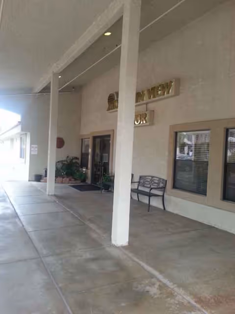 Exterior walkway of Mountain View Manor with a bench and entrance doors.