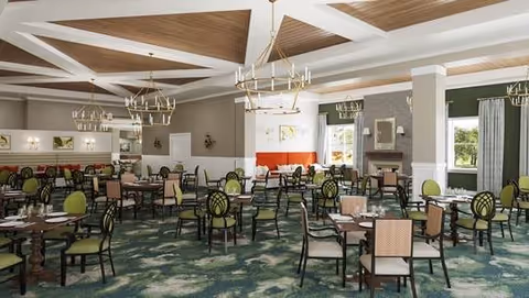 Spacious dining room with multiple tables and chairs arranged neatly. The room features green and beige upholstered chairs, wooden tables set with placemats and napkins, large windows with curtains allowing natural light, chandeliers hanging from a coffered ceiling, and a fireplace in the background.