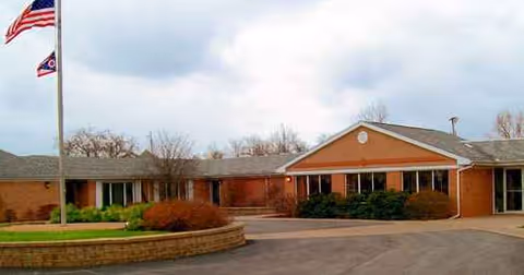 Front exterior of a brick senior living facility with flags and landscaping.