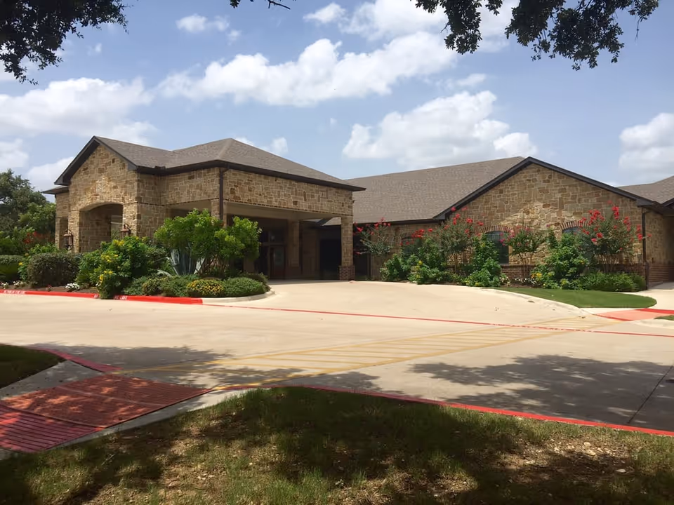Stone-clad senior living center exterior with landscaped entrance and driveway.