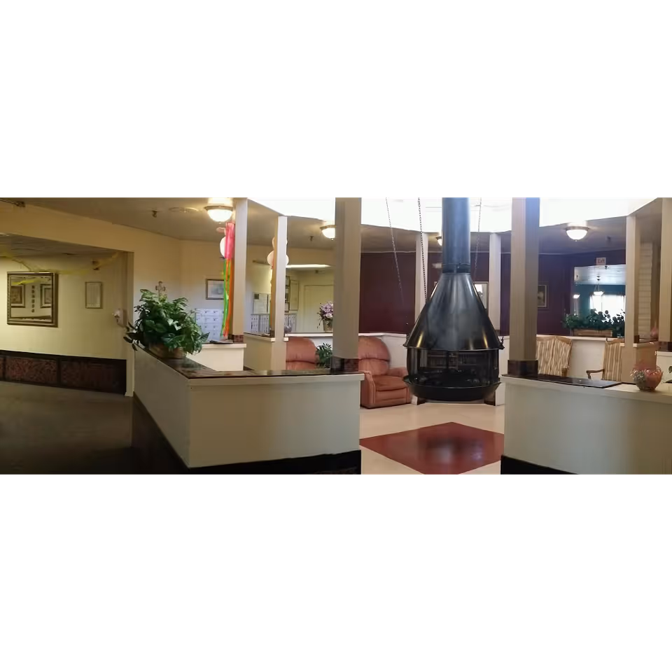 Communal lounge area with a central suspended fireplace, seating, plants, and reception-style partitions.