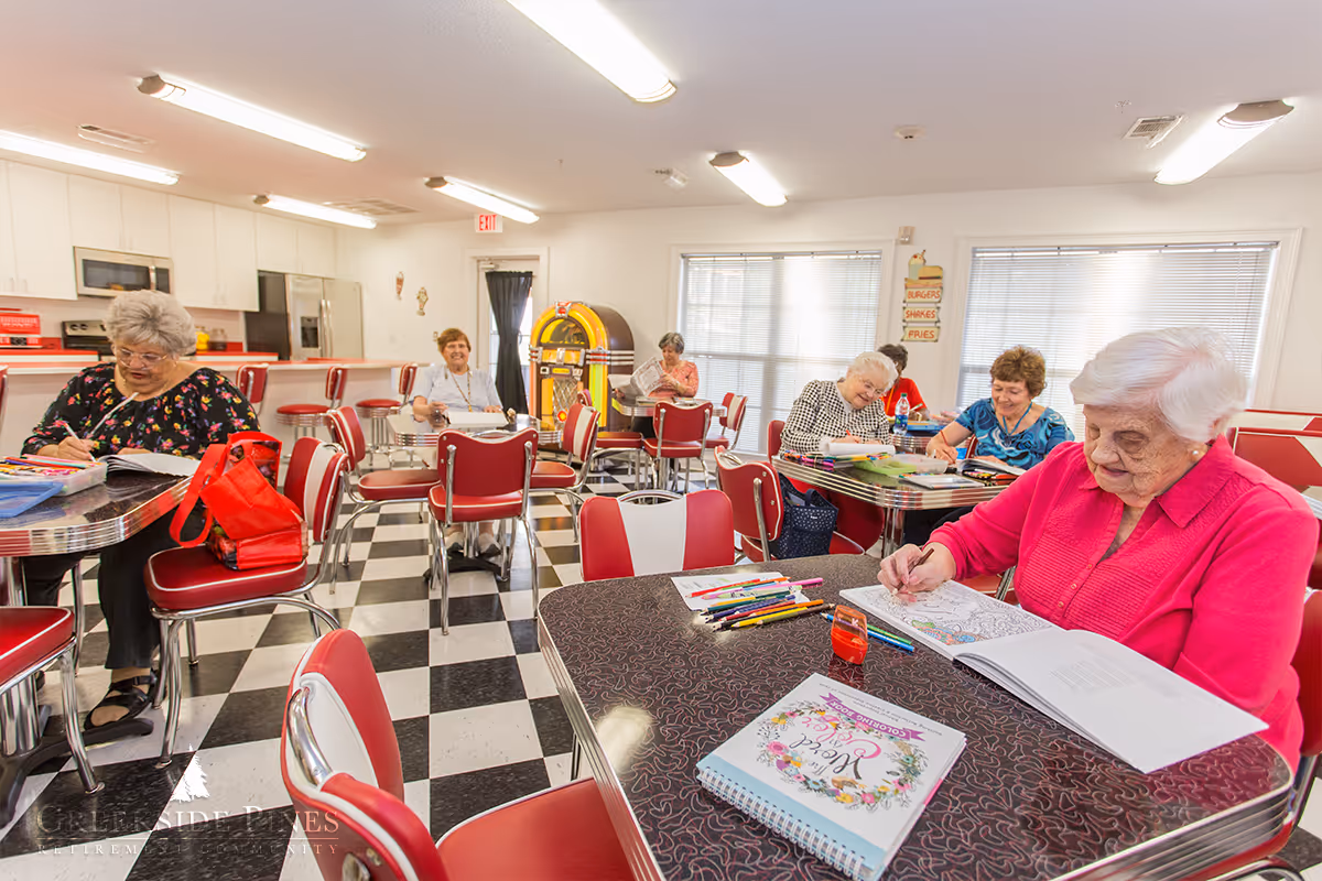 Elderly women sitting at retro diner-style tables coloring and socializing in a common room.