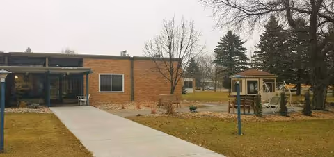 Brick facility exterior with a central walkway, gazebo, and bare trees in a manicured lawn.