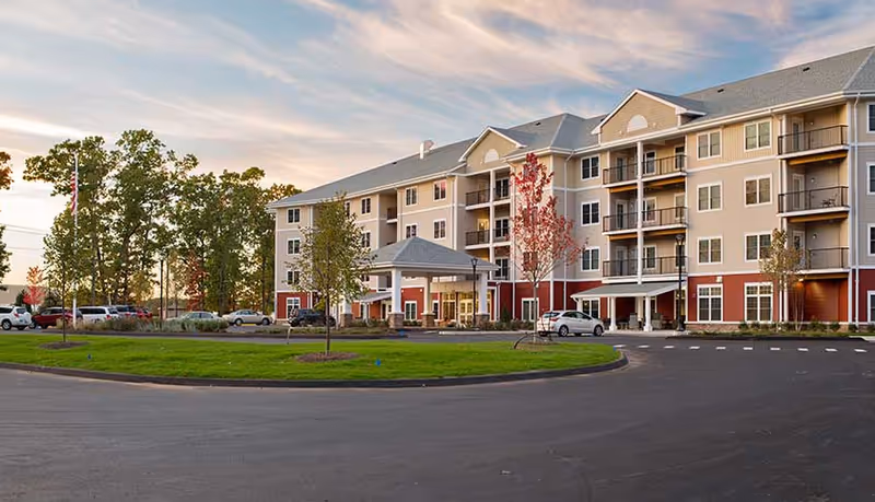 Exterior view of Stonebrook Village at Windsor Locks showing driveway, parking, and entrance canopy.