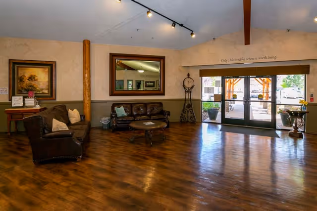 Spacious facility lobby with leather sofas, a coffee table, a large wall mirror, and glass double doors leading outside.
