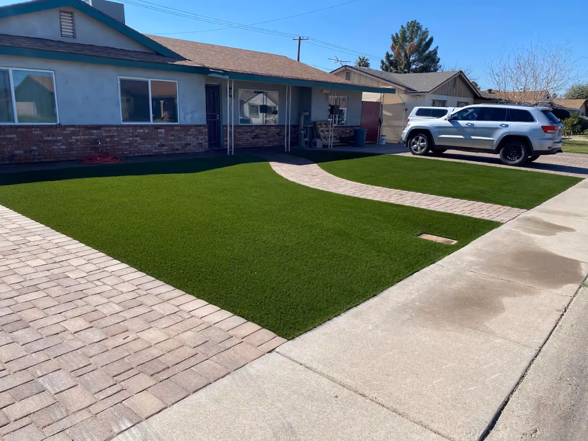 Single-story home's front exterior with a paved driveway, artificial turf lawn, walkway, and a parked SUV.