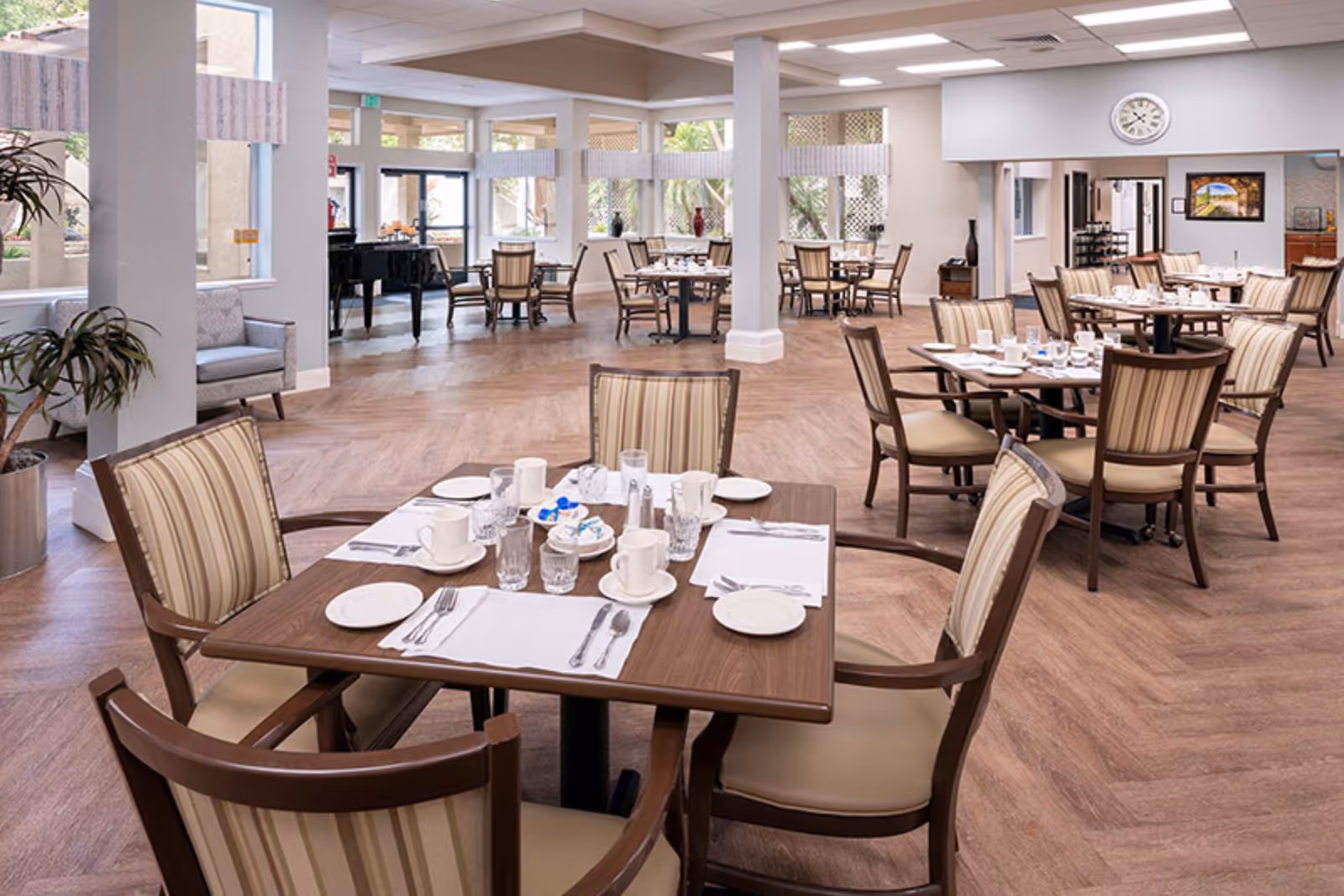 Bright, spacious dining room with several set tables and upholstered chairs on a herringbone wood floor.