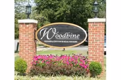 Entrance sign reading 'Woodbine Rehabilitation & Healthcare' mounted between brick pillars with lamps and landscaped flowers in front.