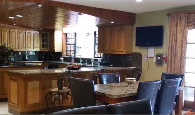 Open kitchen with wooden cabinets, a granite island, and a dining table with upholstered chairs.