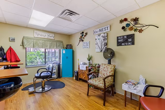 Interior salon-style room with salon chairs, a hooded hair dryer, a teal storage cabinet, and decorative wall art.