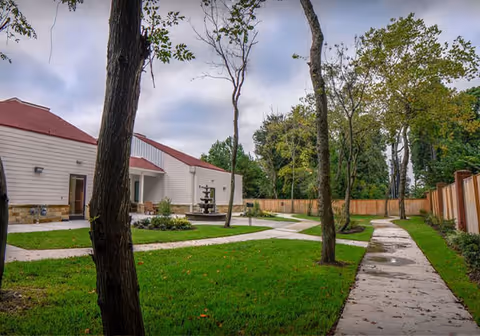 Exterior view of Village Green Memory Care Community Cypress Louetta with lawn and trees