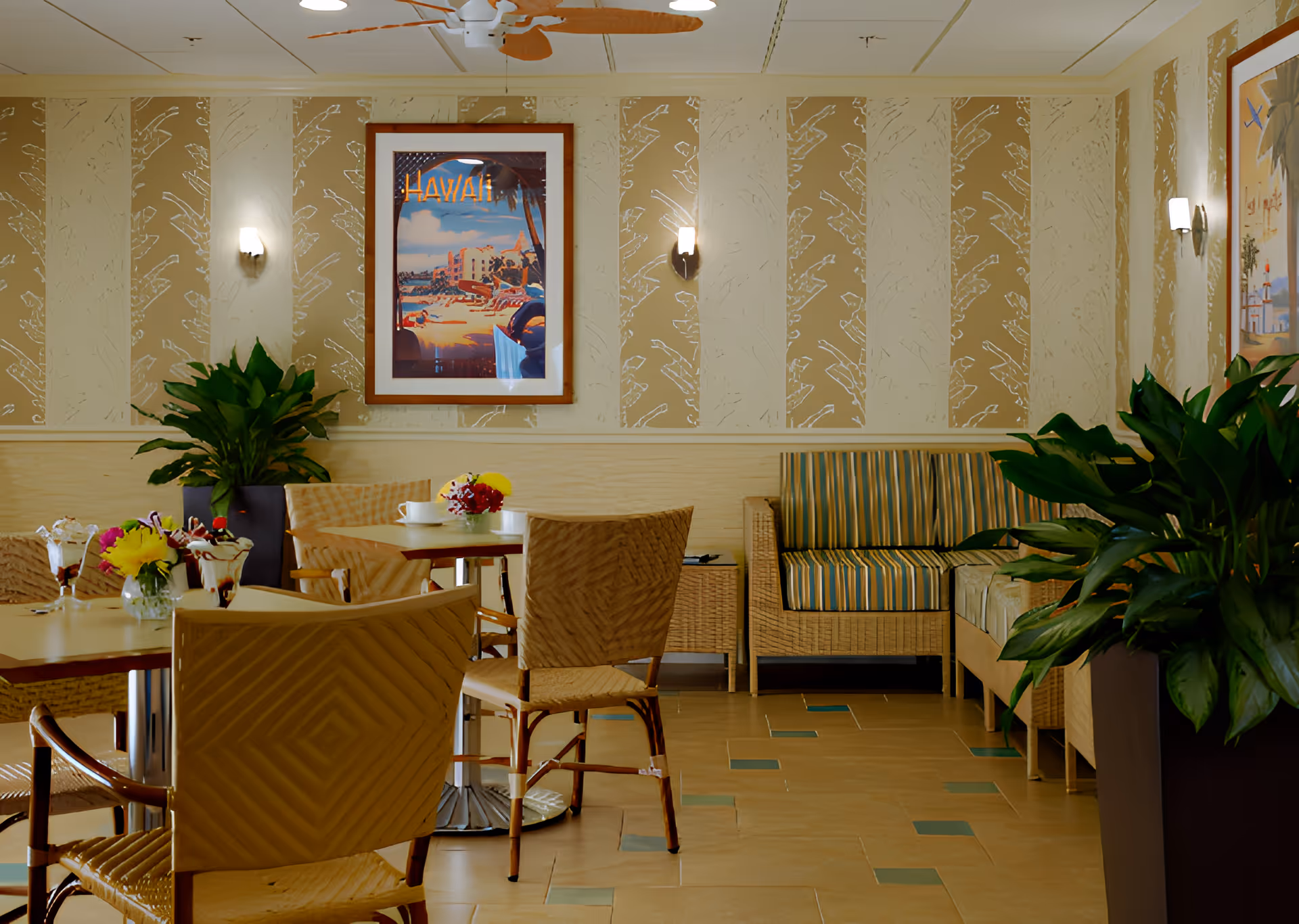 Bright senior living dining area with wicker chairs and tables, potted plants, striped bench seating and framed wall art.