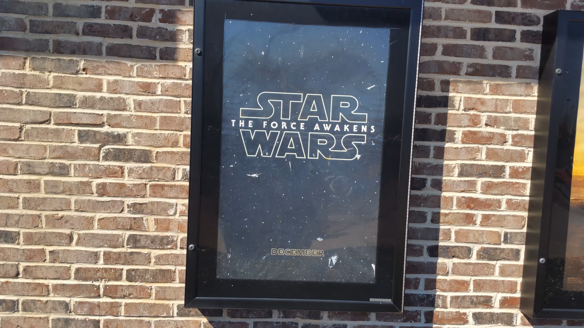 A framed 'Star Wars: The Force Awakens' poster mounted on a brick exterior wall.