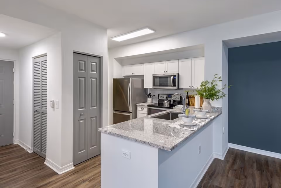 Modern open-concept kitchen with a granite peninsula, stainless steel appliances, white cabinets, and place settings on the bar.