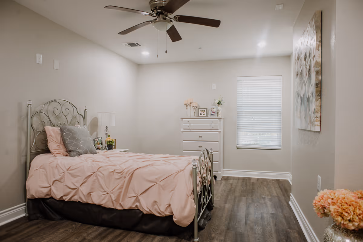 Bright bedroom with a metal-framed twin bed dressed in pink bedding, a dresser, ceiling fan and window.