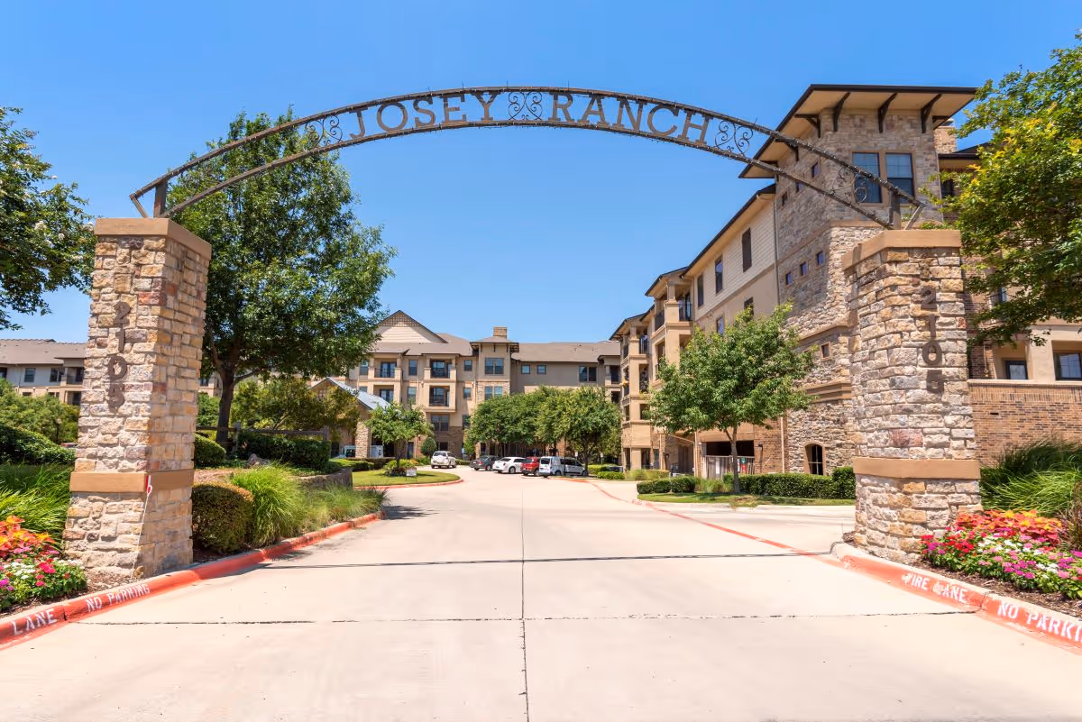 Stone entrance arch reading 'JOSEY RANCH' over a driveway leading to a multi-story senior living building with landscaping.