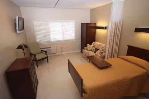 Senior living facility bedroom with bed, sofa, chair, dresser, and window blinds.