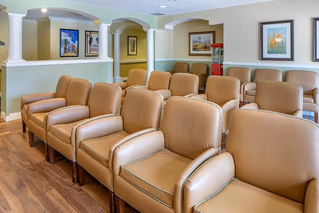 Rows of tan leather armchairs arranged in a common seating area with framed artwork and columns along the walls.