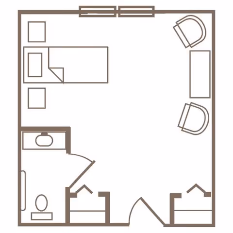Floor plan of a senior living facility room showing a bedroom area with a bed and two chairs with a table, and a bathroom with a toilet and sink.