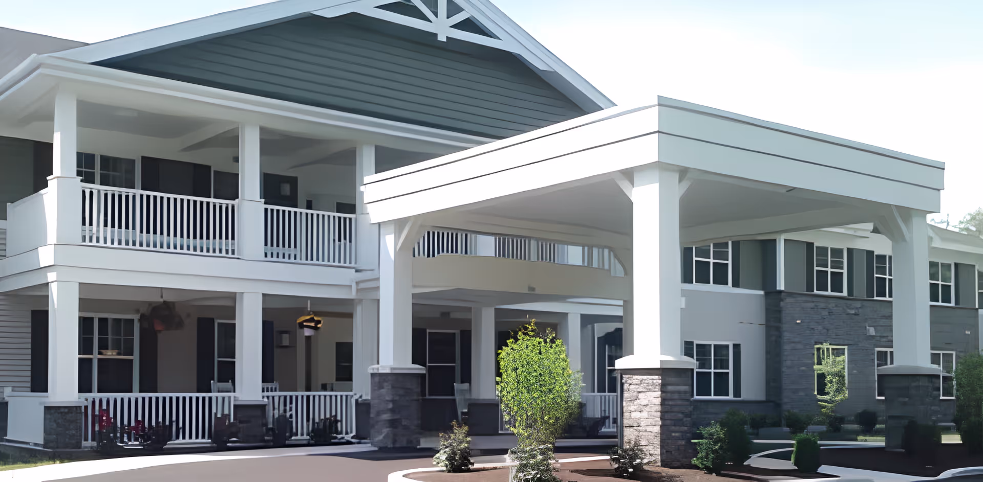 Front entrance of a two-story senior living building with a covered porte-cochere, balconies, and white columns.