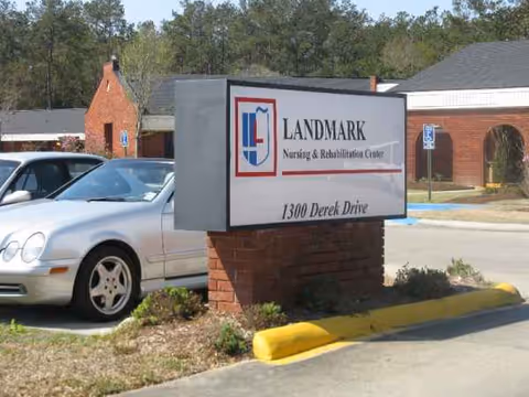 Sign for Landmark Nursing & Rehabilitation Center beside a parked silver car in a parking lot.