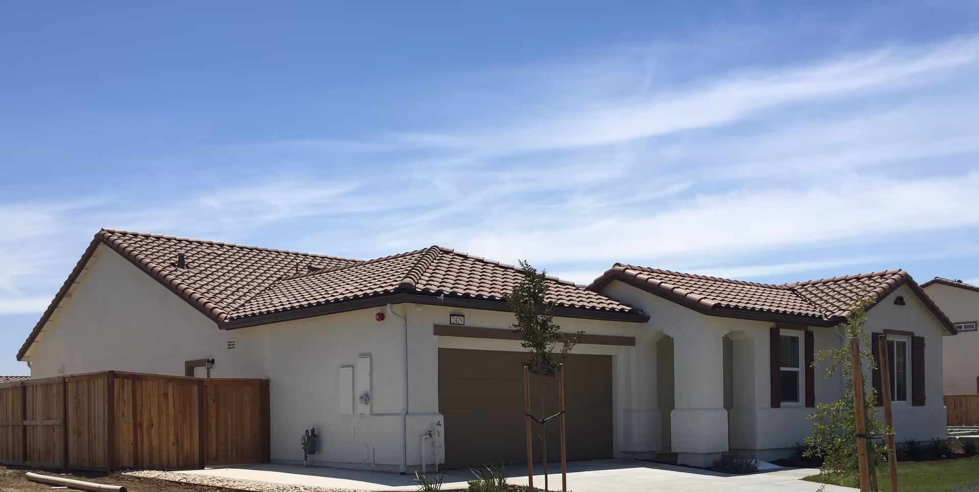 Single-story stucco house with a tiled roof, attached garage and driveway under a blue sky.