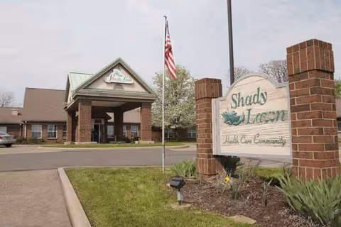 Exterior view of The Oaks at Shady Lawn entrance with brick sign, flagpole, and landscaping.