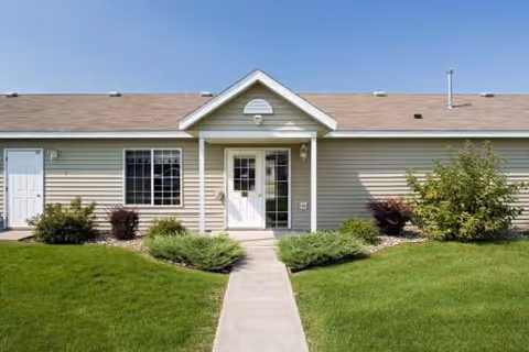 Front entrance of a single-story townhome-style building with a walkway and manicured lawn.
