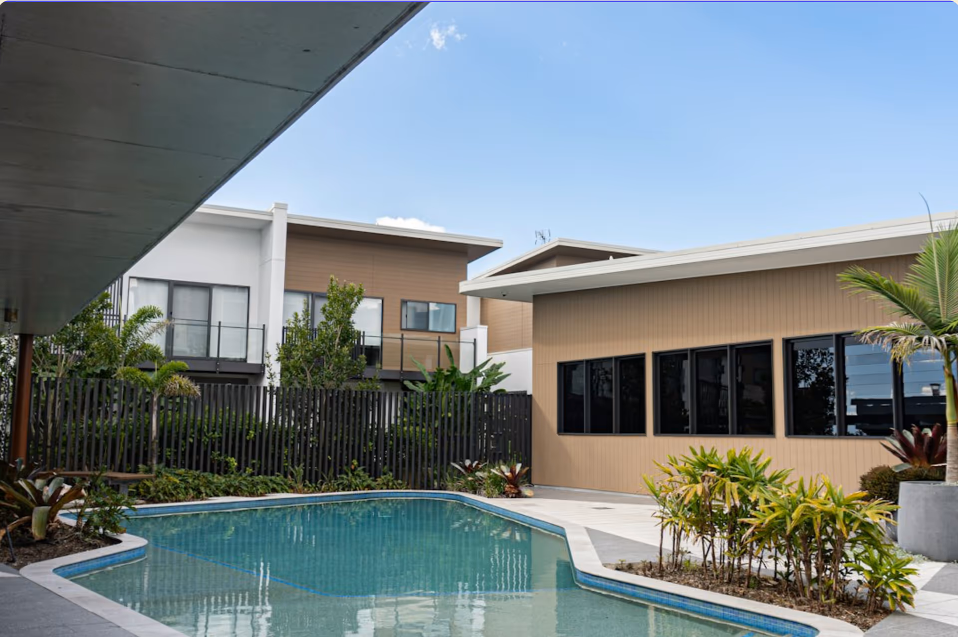 Outdoor courtyard with a swimming pool, plants, and modern residential buildings under a clear blue sky.